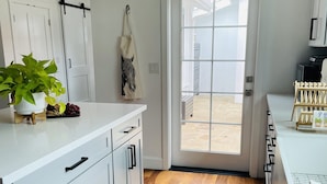 A modern kitchen with white cabinetry, a wooden floor, and a view through a glass door to an outdoor area.