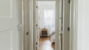 A hallway with wooden flooring leading to a bedroom with a bed and a nightstand.