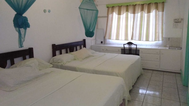 A room with two beds, a window with striped curtains, and mosquito nets on the wall. - 4 separate single bedrooms,bathrooms,living and kitchen.beach access (Rodney Bay)