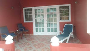 A covered patio area with two blue lounge chairs and a wooden table, a red wall, and a glass door with a grid pattern. - 4 separate single bedrooms,bathrooms,living and kitchen.beach access (Rodney Bay)