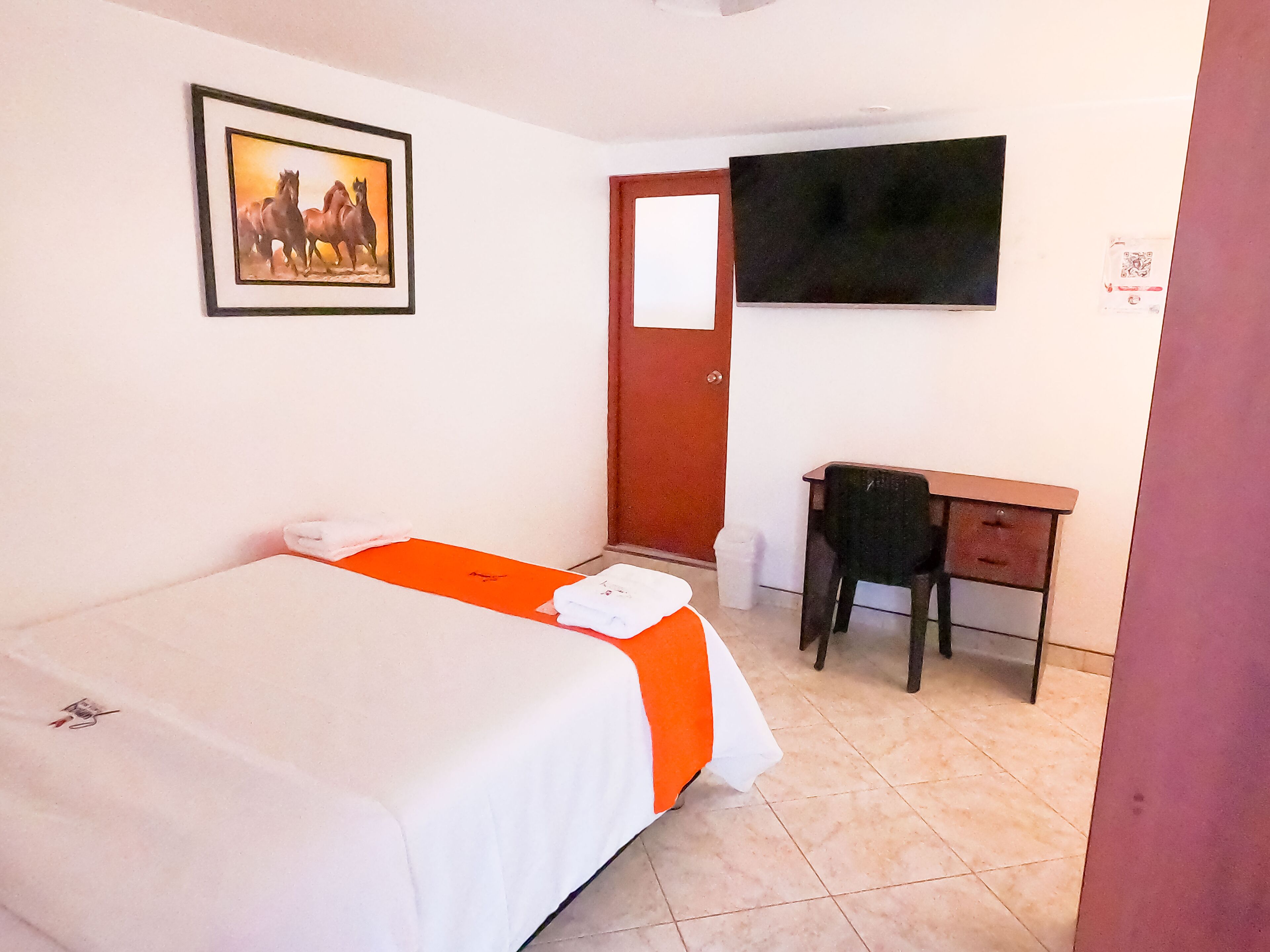 Habitación de hotel con cama, escritorio, silla, televisor y puerta.