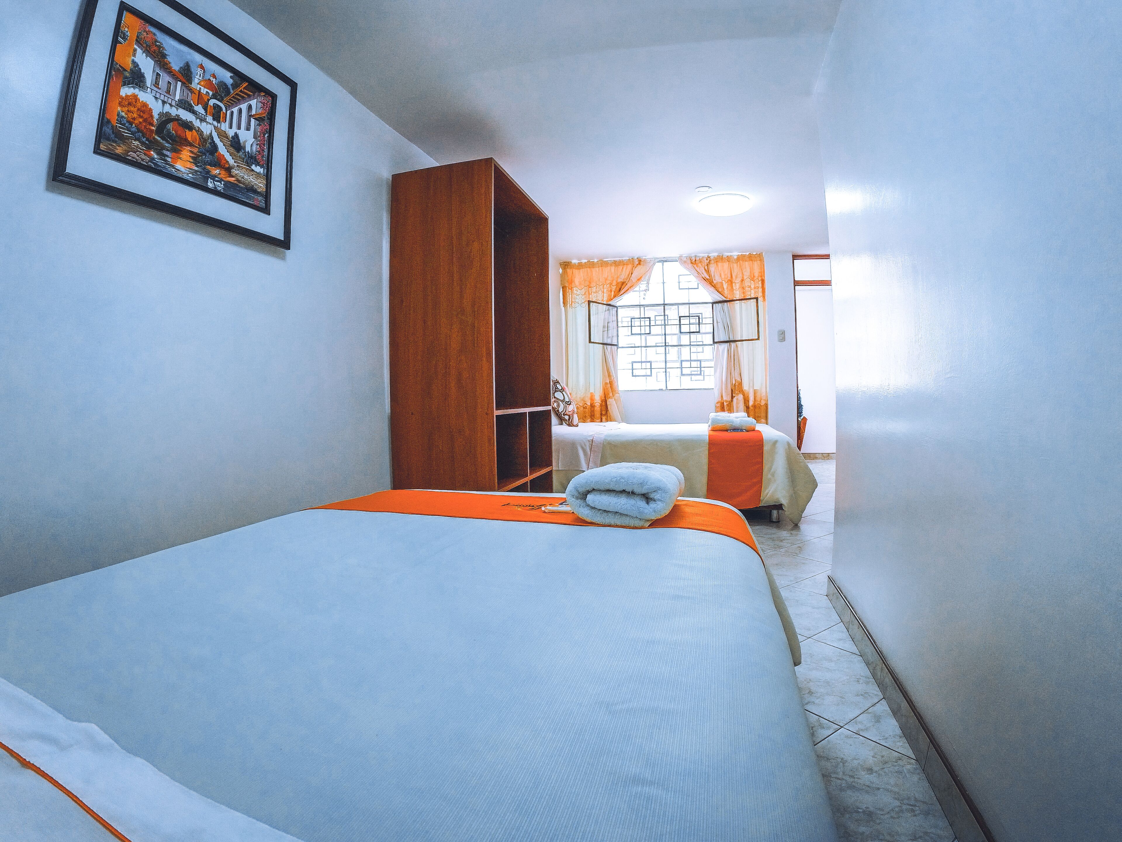 Een hotelkamer met twee bedden, een houten garderobe, een schilderij aan de muur en een raam met gordijnen.