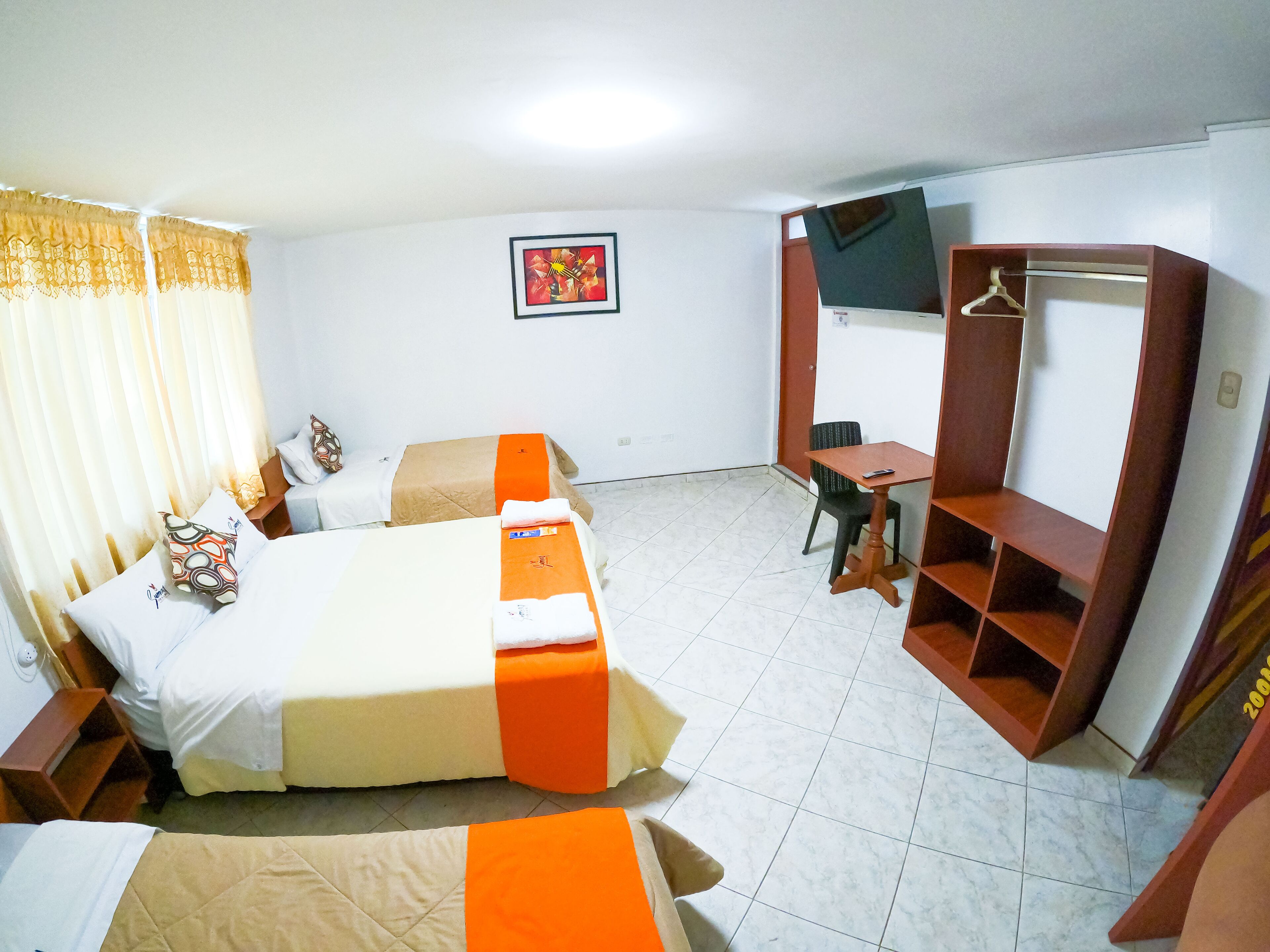 A hotel room with two beds, a desk, a chair, a wardrobe, and a framed picture on the wall.