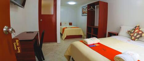 A hotel room with a bed, a desk, a chair, a wardrobe, and a television.