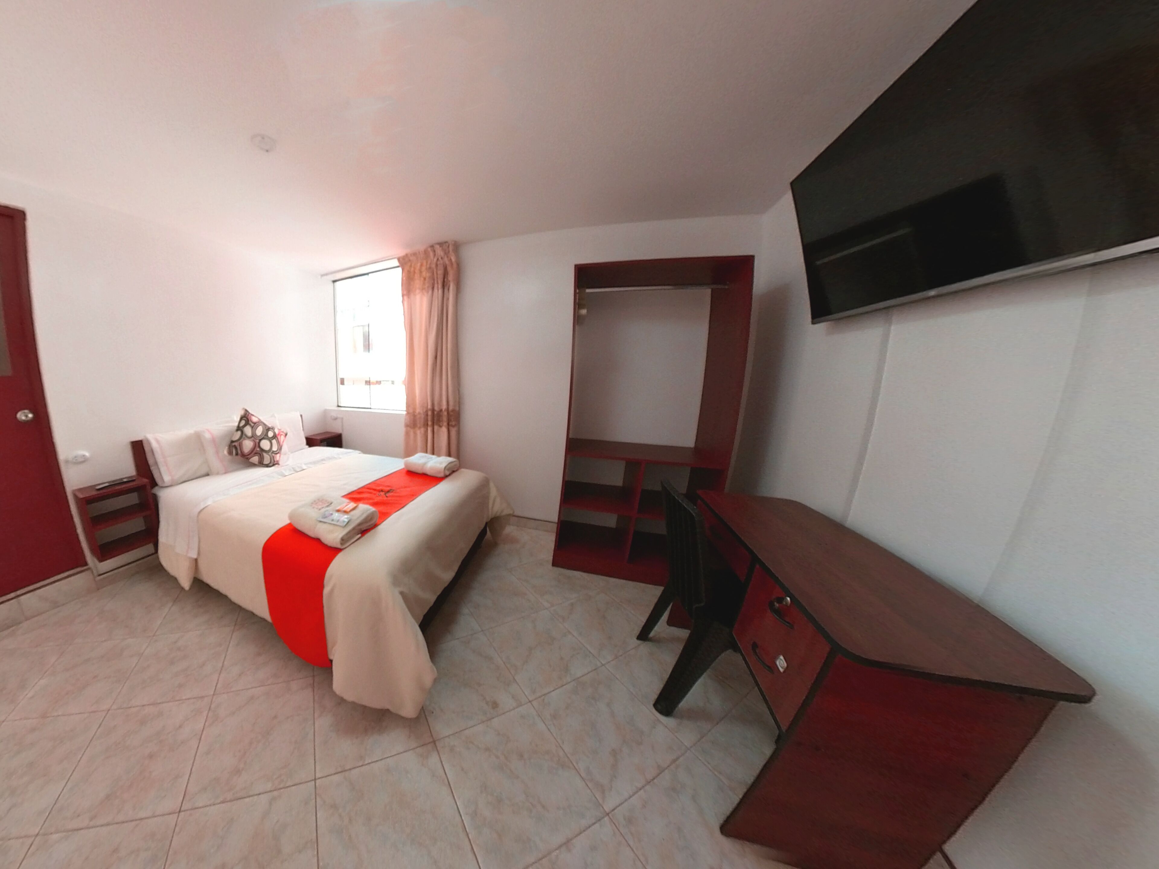 Habitación de hotel con cama, escritorio, televisión y ventana con cortinas.