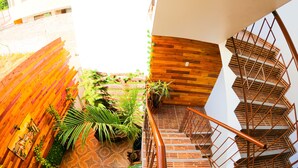 Una escalera de caracol con detalles de madera y barandillas de metal, rodeada de plantas de interior y un suelo con diseño.