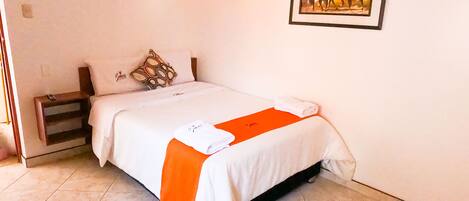 A neatly made bed with a white and orange bedspread, a pillow with a geometric pattern, and a framed picture of horses on the wall.