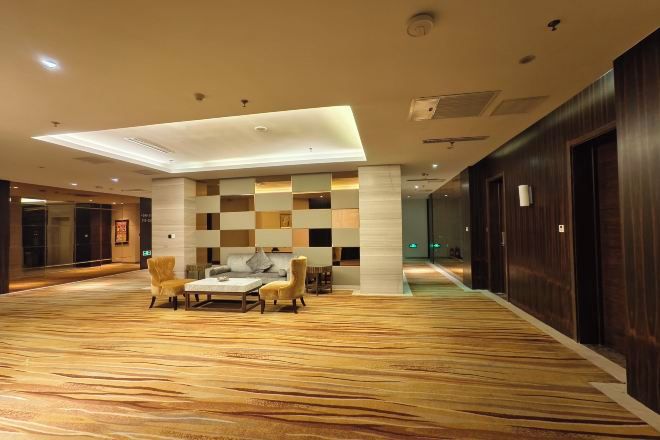 A spacious lobby with a checkered wall pattern, a wooden floor, and a seating area with chairs and a table.