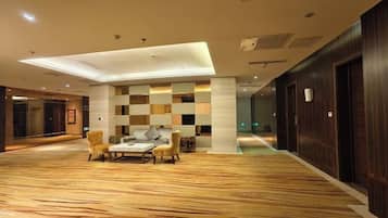 A spacious lobby with a checkered wall pattern, a wooden floor, and a seating area with chairs and a table.