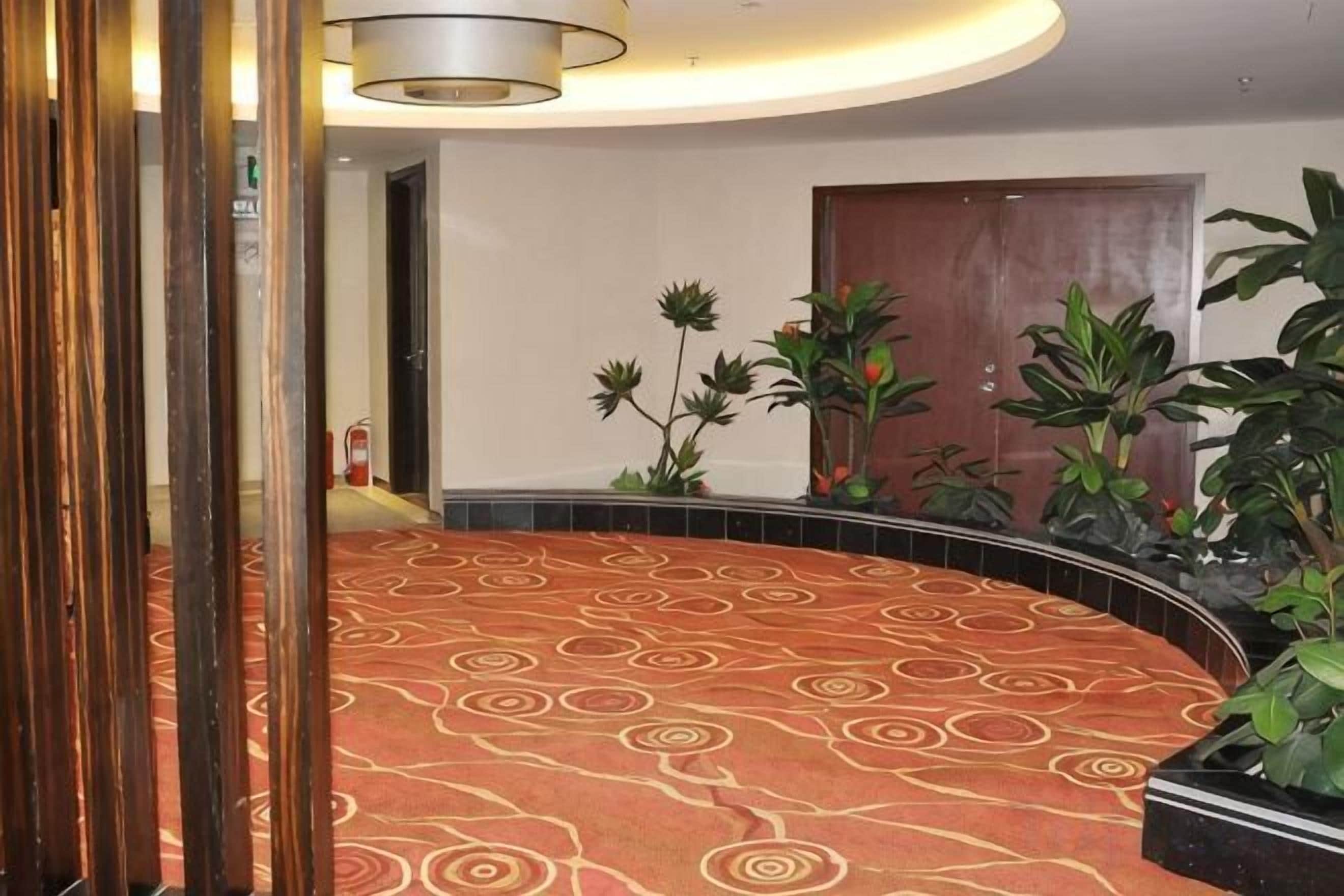 A hotel lobby with a patterned carpet, a wooden door, and potted plants.