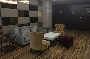 Habitación de hotel con sofá, sillones, una pequeña mesa y alfombra estampada.