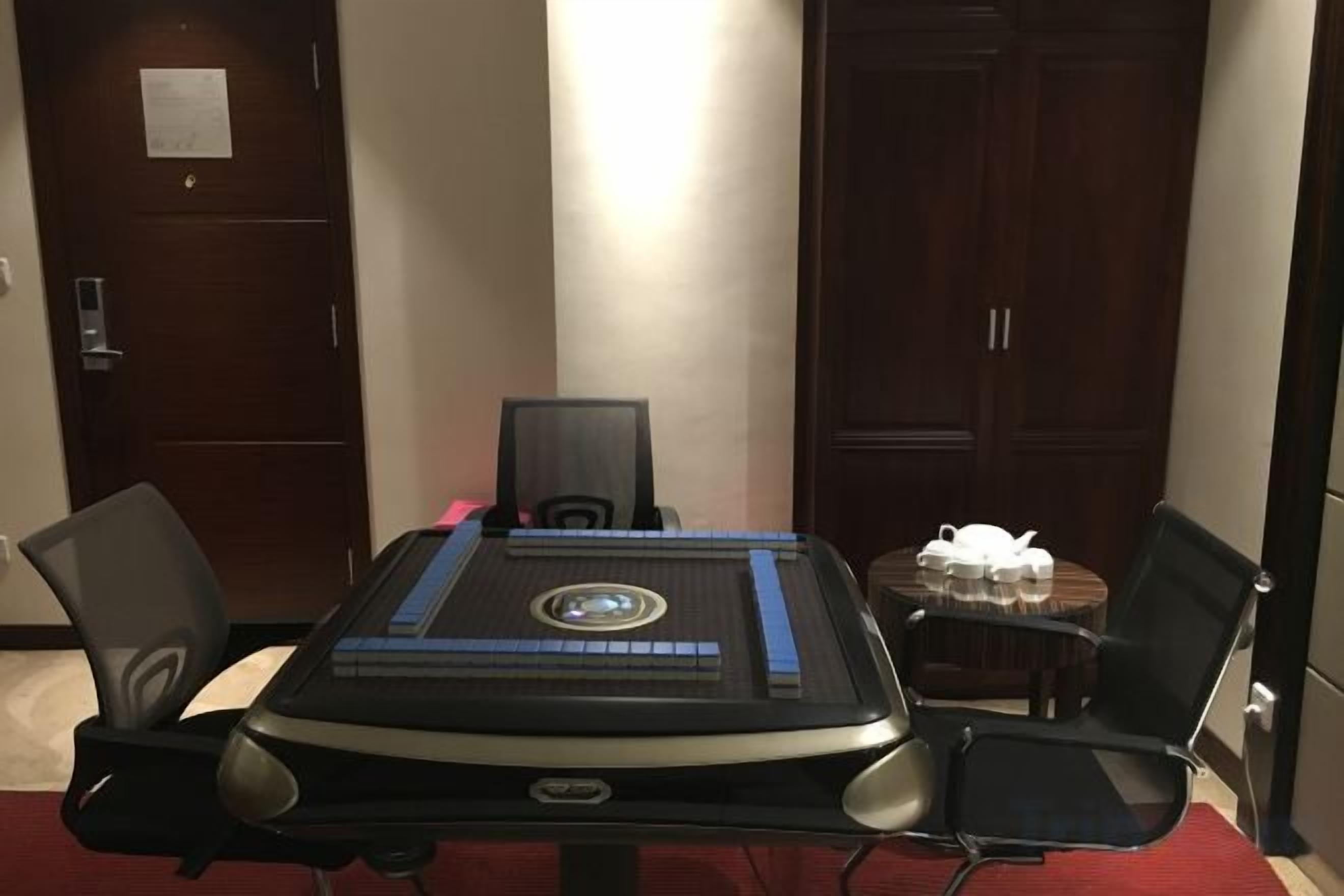 Une table de conférence dotée d’un panneau de contrôle central, entourée de quatre chaises, dans une pièce aux portes en bois et au tapis rouge.