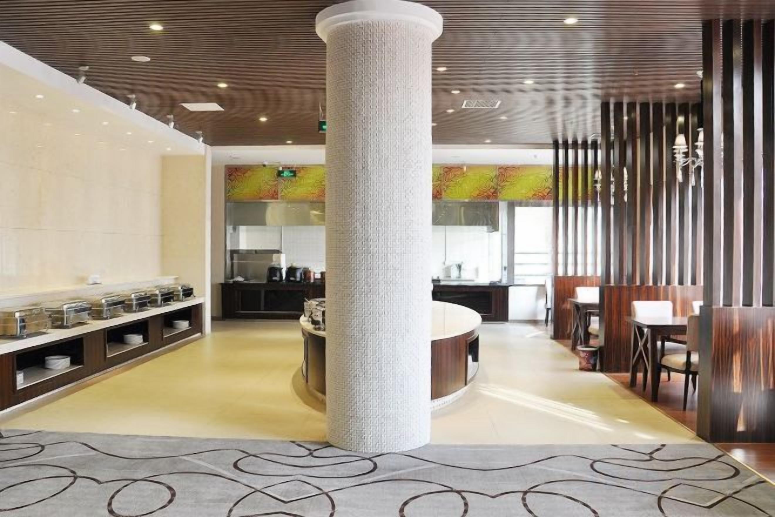 Un hall d’hôtel doté d’une colonne centrale, d’un espace buffet et d’un coin salon avec des tables et des chaises.