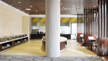 Un hall d’hôtel doté d’une colonne centrale, d’un espace buffet et d’un coin salon avec des tables et des chaises.