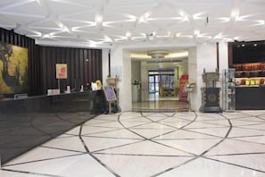 A hotel lobby with a reception desk, a large abstract painting, and a tiled floor.