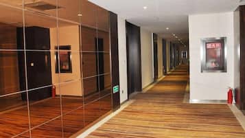 A hotel corridor with mirrored walls, a patterned carpet, and a fire extinguisher on the right.