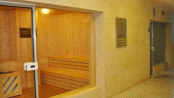 A sauna with a wooden bench and a glass door, adjacent to a wall with a plaque and a door.