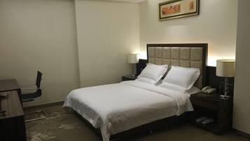 Una habitación de hotel con una cama, mesitas de noche, un escritorio y una silla.