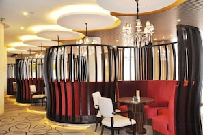 A restaurant with round tables and booths, a patterned carpet, and a modern chandelier.