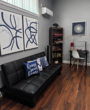 A modern living room with a black leather sofa, abstract wall art, a bookshelf, and a gaming table. - L&J Brand New Jax Studio!!! (Jacksonville)