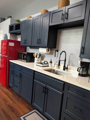A kitchen with dark cabinets, a red refrigerator, a microwave, a coffee maker, and a sink. - L&J Brand New Jax Studio!!! (Jacksonville)
