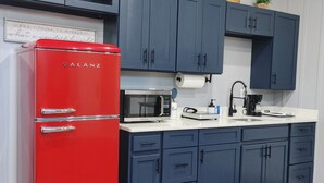 Een keuken met een rode Galanz-koelkast, donkerblauwe kastjes, een witte aanrechtblad en een magnetron.
