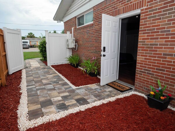 A brick house with a white door, a small garden with mulch and plants, and a stone pathway leading to the door. - L&J Brand New Jax Studio!!! (Jacksonville)