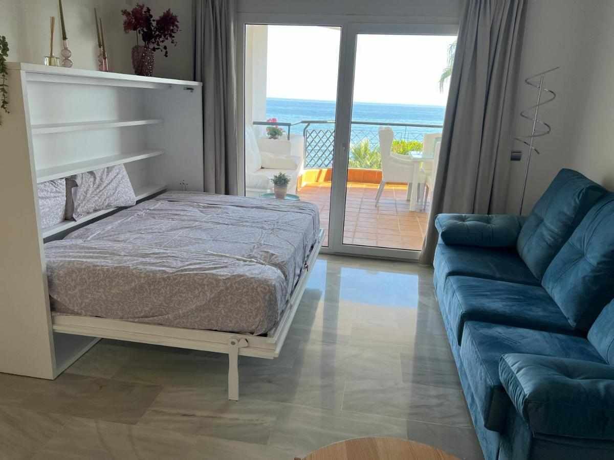 Une chambre à coucher avec un lit, un canapé bleu, un balcon donnant sur la mer et une armoire blanche.