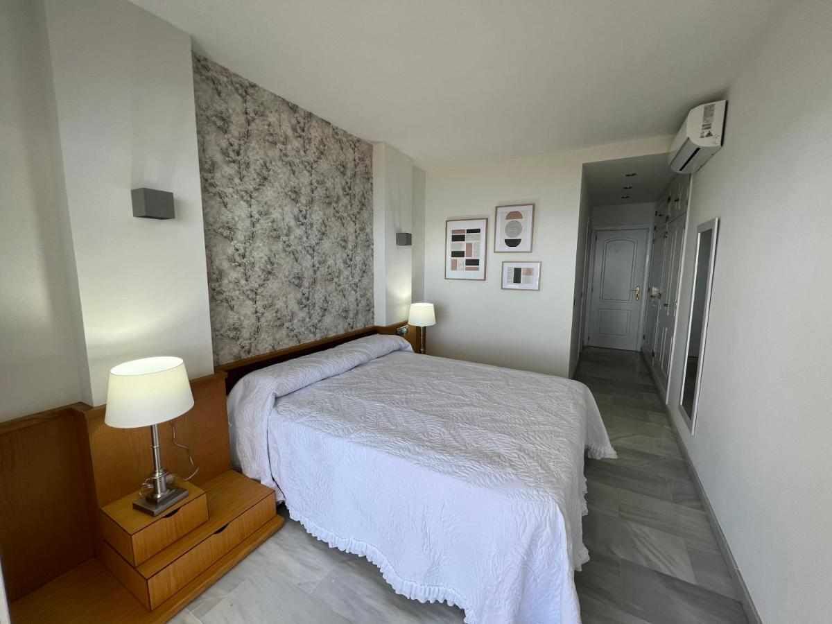 Ein Hotelzimmer mit Bett, Nachttisch, Lampe und einer Wand mit gerahmten Bildern.