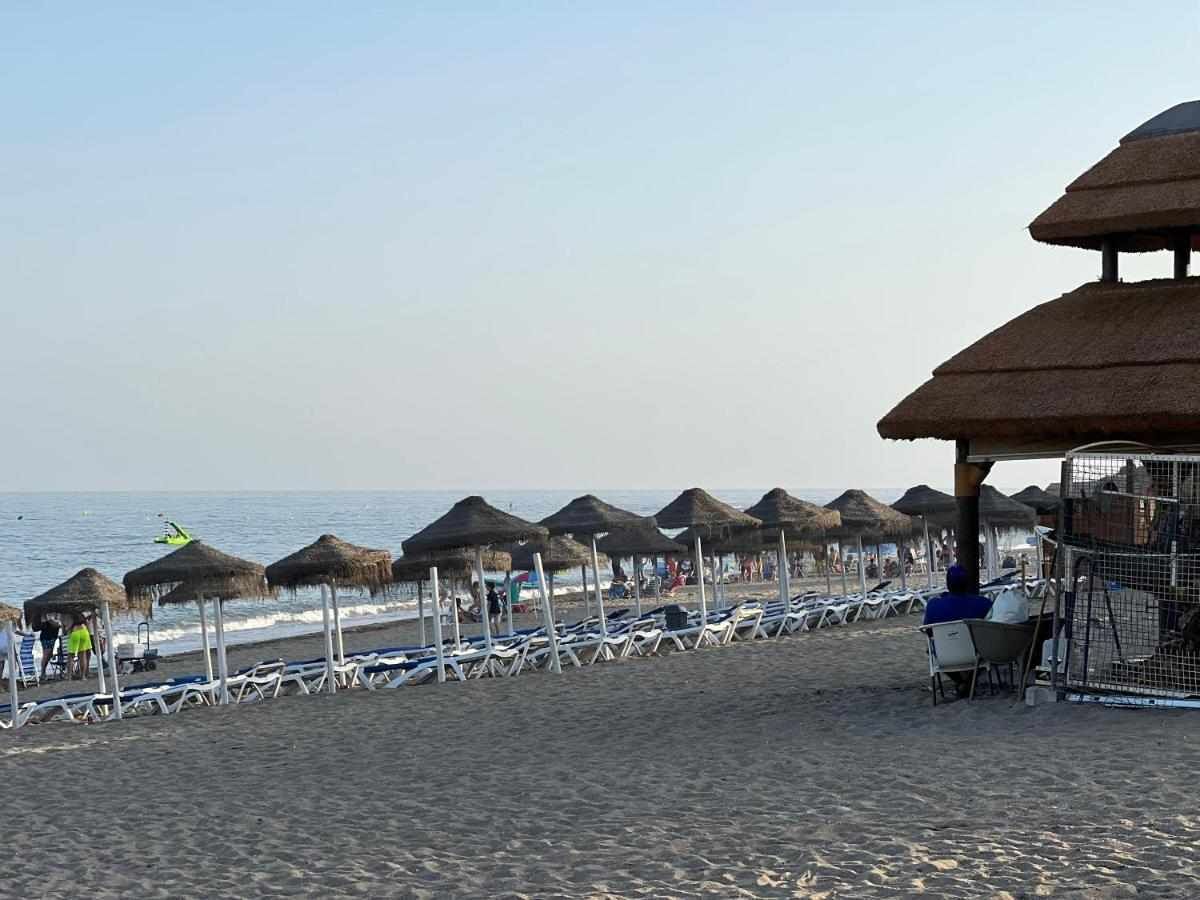 A beach with rows of sun loungers and thatched umbrellas, a fenced area, and a clear view of the sea.