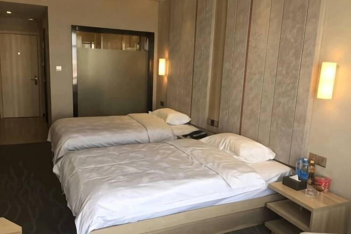 Une chambre d’hôtel avec deux lits, un mur recouvert de panneaux en bois, une table de chevet avec une lampe et une porte.