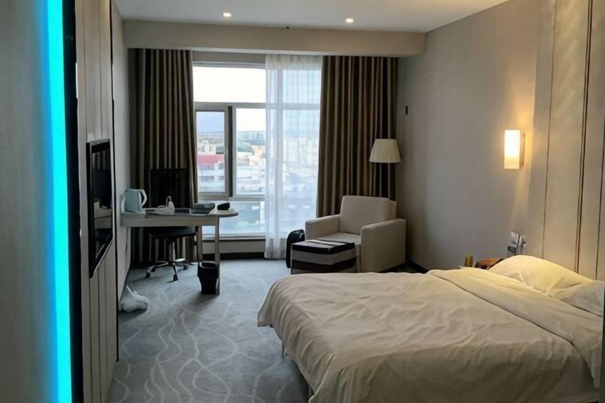 Une chambre d’hôtel avec un lit, un bureau, une chaise et une vue sur la ville par la fenêtre.