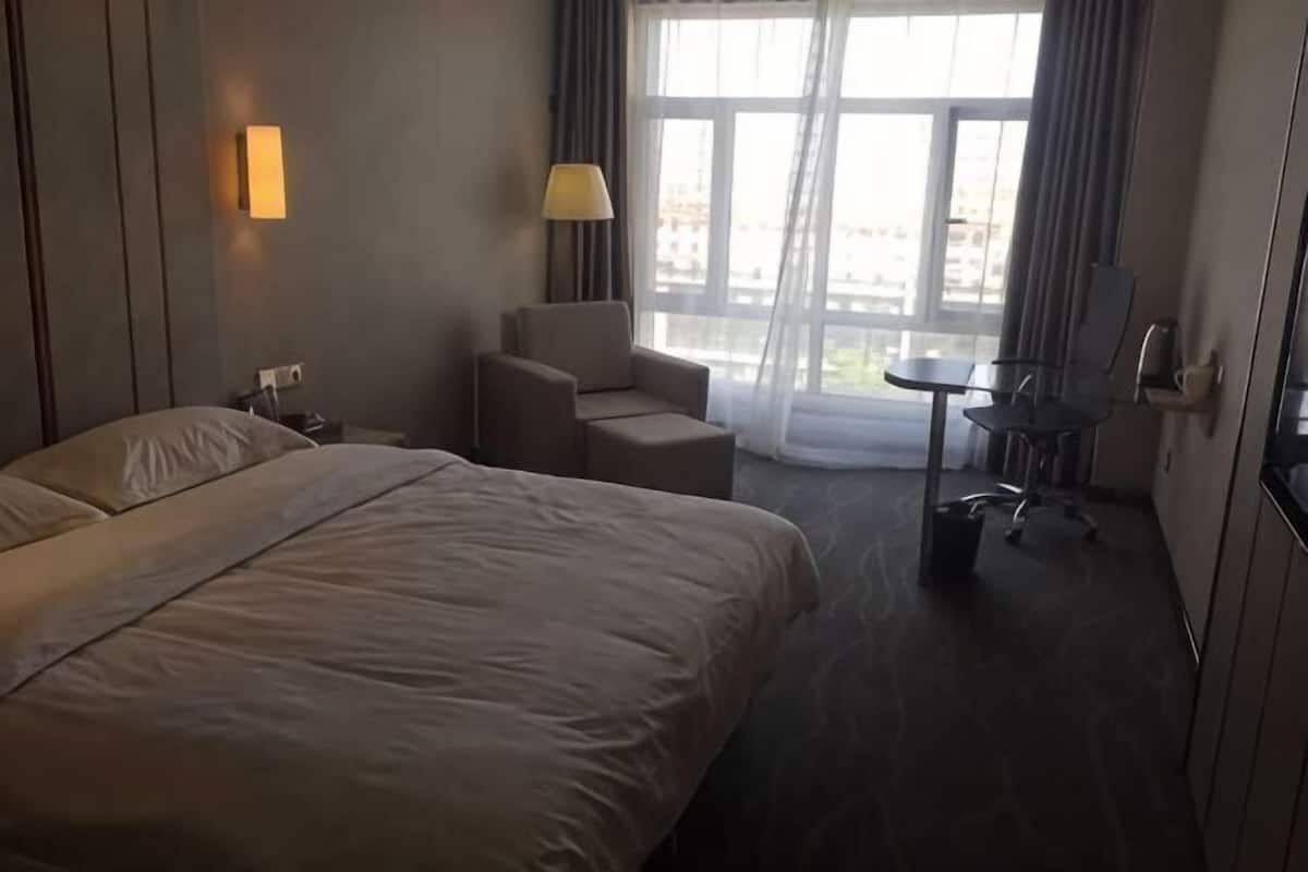 Une chambre d’hôtel avec un grand lit, un bureau, une chaise, une lampe et une vue par la fenêtre.