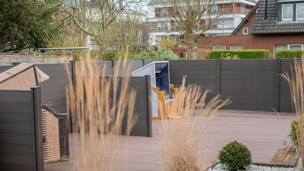 A modern outdoor patio with a wooden bench, a metal gate, and a view of residential buildings in the background.