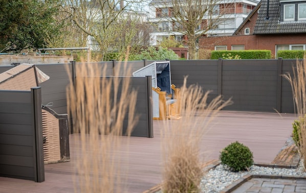 A modern outdoor patio with a wooden bench, a metal gate, and a view of residential buildings in the background.