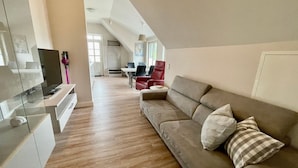 A modern living room with a sofa, a TV, and a dining area in the background.