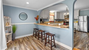 Una cocina con pared azul, taburetes de bar de madera, un espejo redondo y un estante de madera con un letrero que dice 'HOMEMADE'.