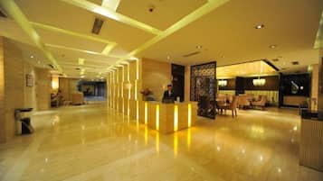Un vestíbulo de hotel con mostrador de recepción, zona de estar y un separador decorativo.