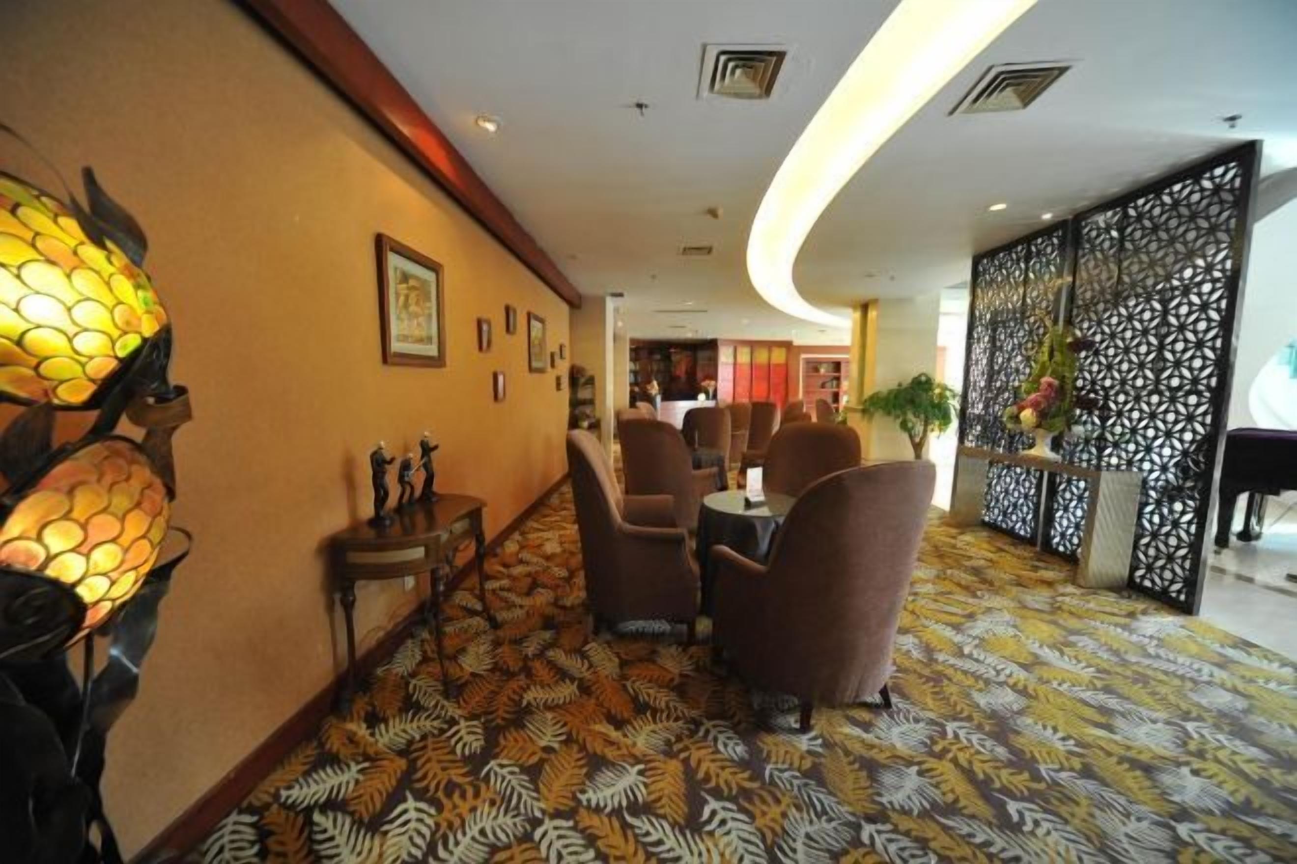 A hotel lobby with a patterned carpet, seating area, decorative wall lamps, and a reception desk.