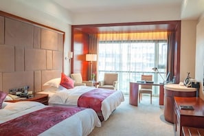 A hotel room with two beds, a desk, a chair, and a large window.