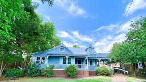 Une maison à deux étages, avec une façade bleue, un porche à l’avant et des fondations en briques.