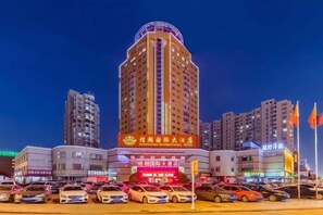 Ein mehrstöckiges Hotel mit einer markanten Schilderfassade, umgeben von anderen Gebäuden und einem Parkplatz.