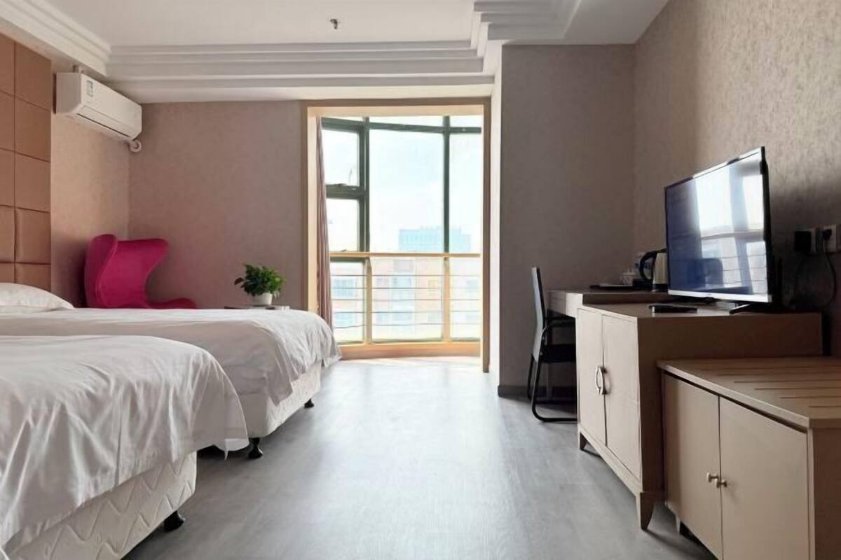 Hotellihuone, jossa on kaksi sänkyä, televisio, työpöytä ja suuri ikkuna.