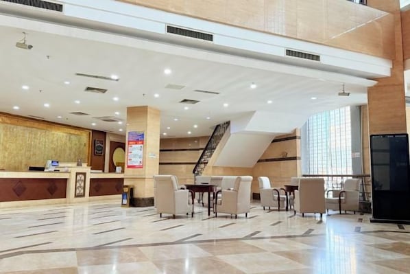 A hotel lobby with a reception desk, seating area, and a staircase.