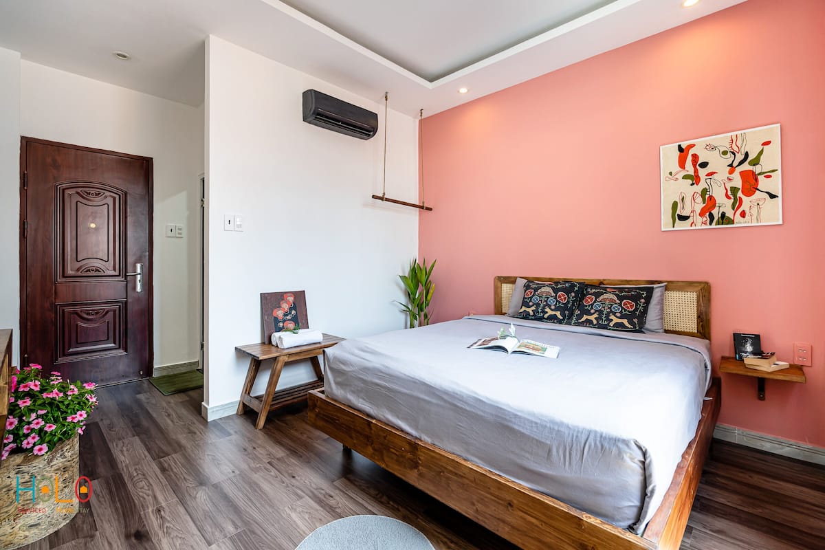Une chambre avec un lit en bois, une table de chevet ornée d’une plante, un climatiseur fixé au mur et une porte.