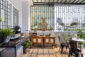 Enjoy a meal at the outdoor dining area with a kitchenette, sink, and kettle, surrounded by lush greenery and a city view.