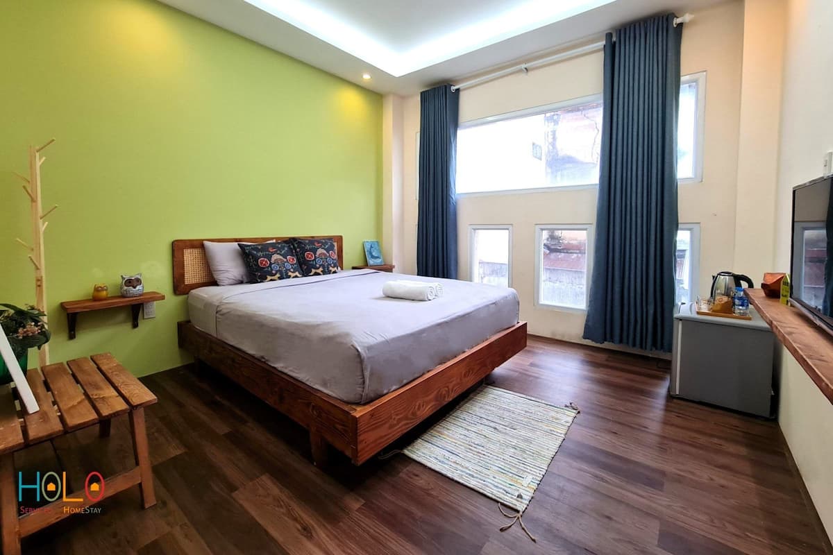 Une chambre moderne avec un lit en bois, une petite table de chevet, une commode, un téléviseur et une fenêtre avec des rideaux.