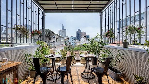 Terraço no telhado com mesas, cadeiras, plantas em vasos e vista da cidade.
