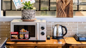 A kitchen area with a microwave, a kettle, and a wooden cabinet. There is a sign with the word "HOLIDAY" and a plant on top of the microwave.
