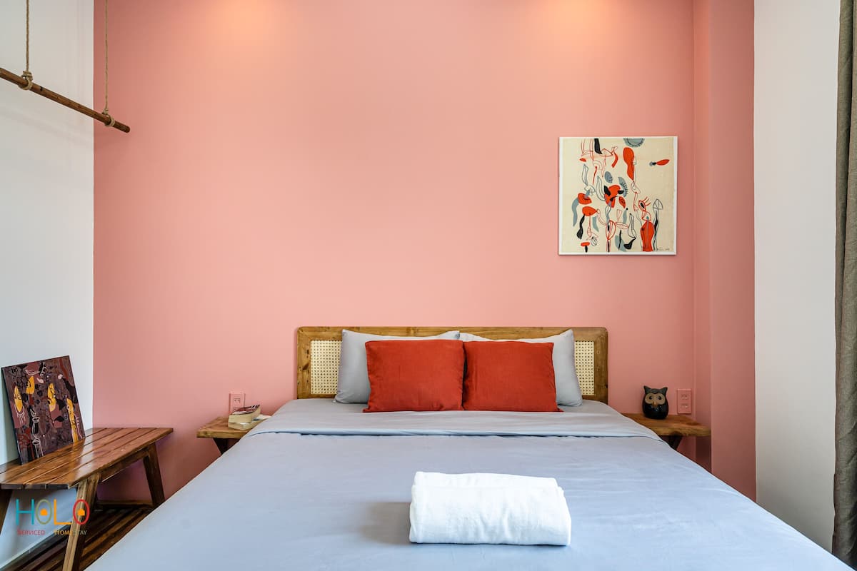 Une chambre à coucher bien rangée, avec un lit, des oreillers, une table de chevet et une œuvre d’art accrochée au mur.